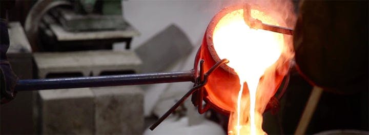 A crucible of molten bronze being poured in a ceramic mold